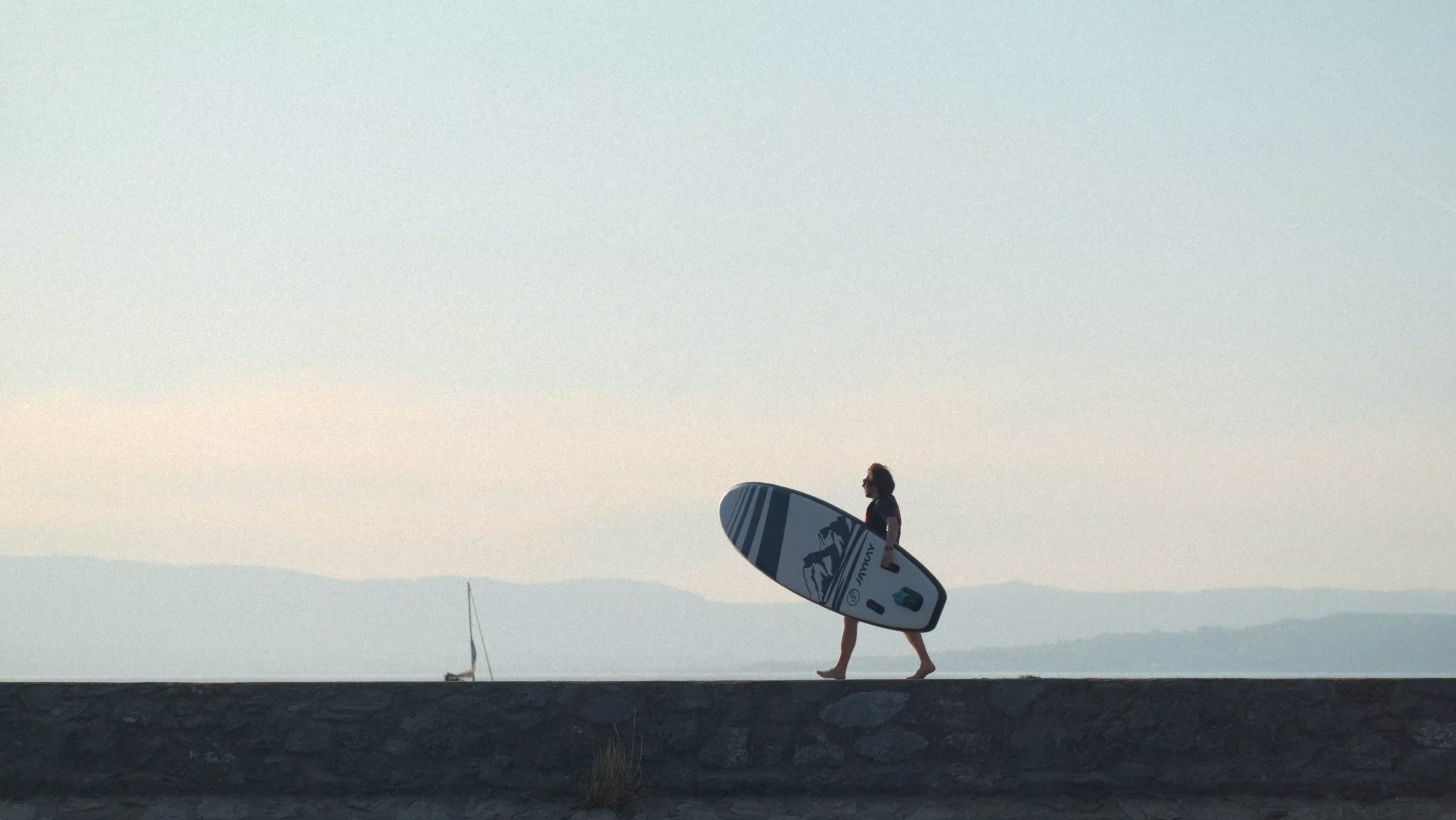 Frau trägt SUP-Board vor Landschaft